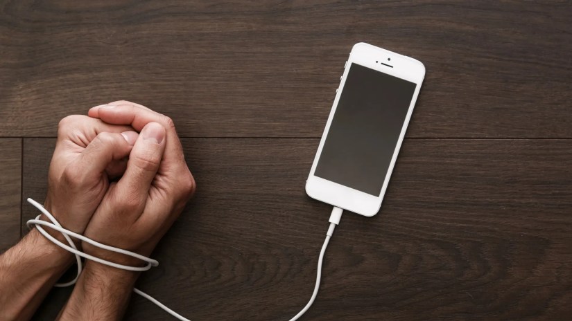 Person&rsquo;s hands tied up by a phone charging cable.