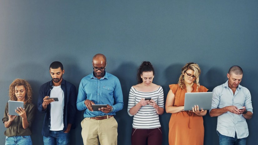 Row of people staring at smartphone, tablet, and laptop screens.