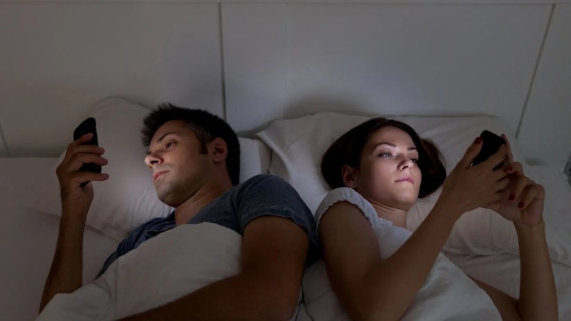 Two people in bed on their smartphones.