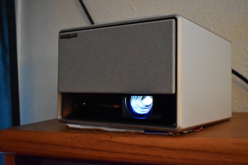 The XGIMI Horizon Ultra placed upside-down on a bookshelf with some cardboard shoved under it to get the right projection angle.