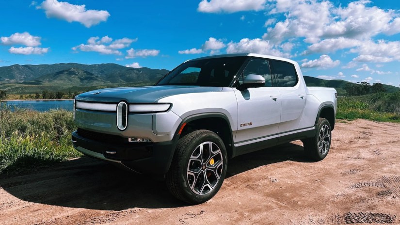 Rivian&rsquo;s R1T electric truck is parked off-road by a lake in the mountains.