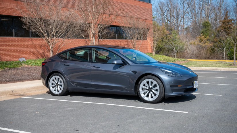 A Tesla Model 3 from the side in a parking lot.