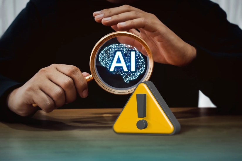 A person with a magnifying glass with the text &lsquo;AI&rsquo; and a warning icon.