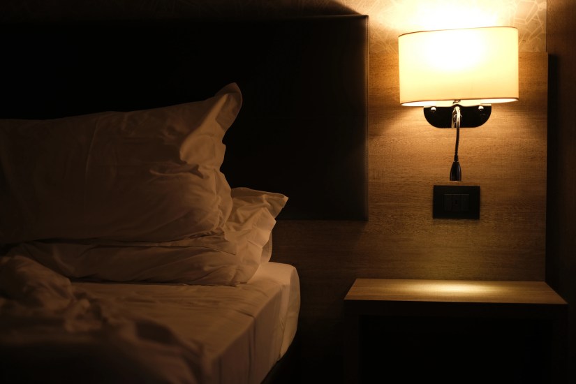 Beside lamp emitting soft, warm light on the bed.