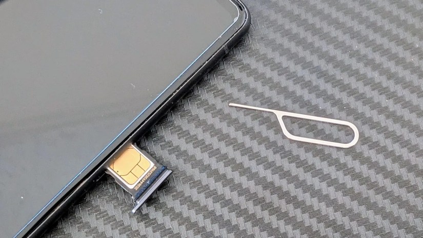 A SIM tool next to a  smartphone with the SIM card visible in its tray.