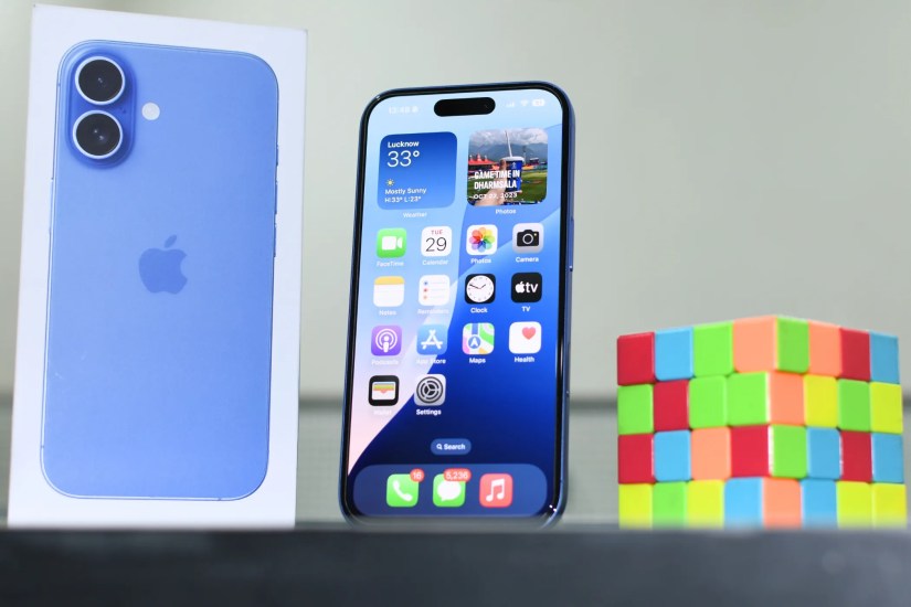 iPhone 16 on a shelf with its box on the left and a rubik&rsquo;s cube on the right.