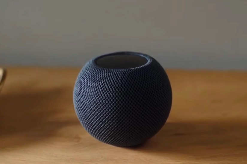 Black HomePod Mini sitting on a wooden table top.