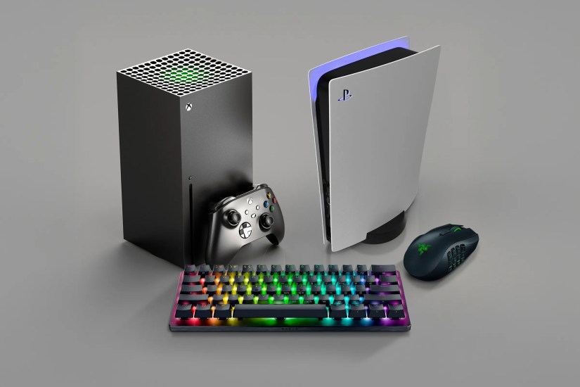 An Xbox next to a PlayStation, with a keyboard and mouse beside them.
