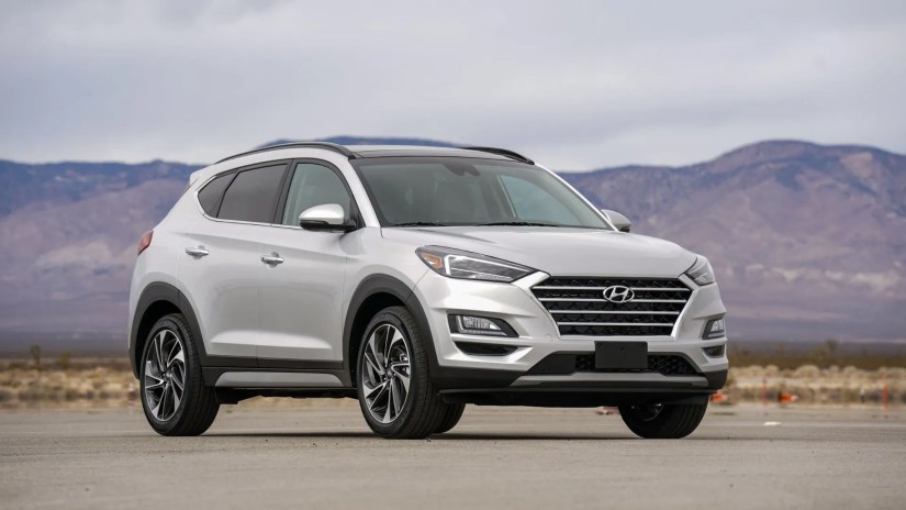 Full view of silver 2021 Hyundai Tuscon Hybrid parked on tarmac with moutains in the background.