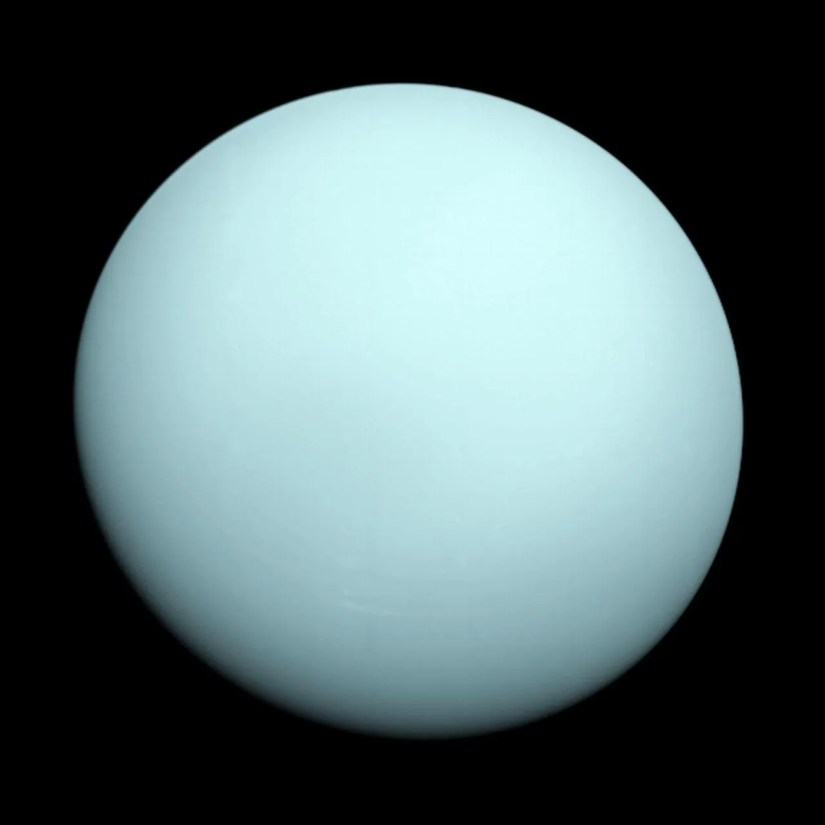 The greenish-blue planet Uranus seen in the blackness of space.