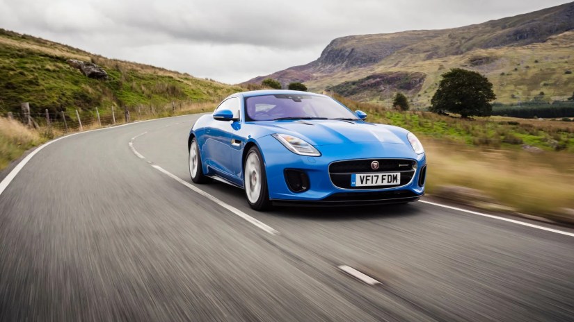 Front 3/4 view of blue 2017 Jaguar F-TYPE driving on a winding country road in the UK.