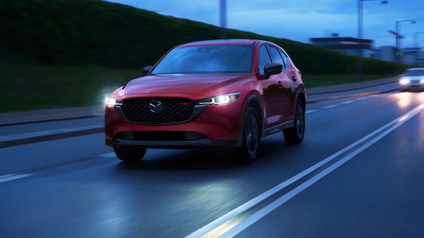 Front three-quarter view of a red 2025 Mazda CX-5 driving at night through a city.