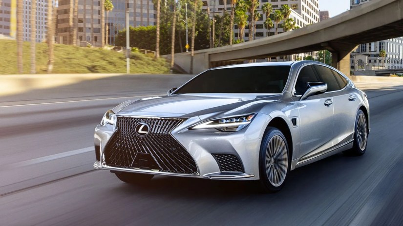 Front three-quarter view of a silver 2025 Lexus LS 500h driving through a city.