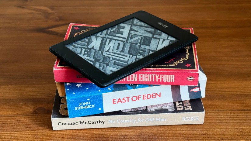 A stack of books with a Kindle eReader on top of them.