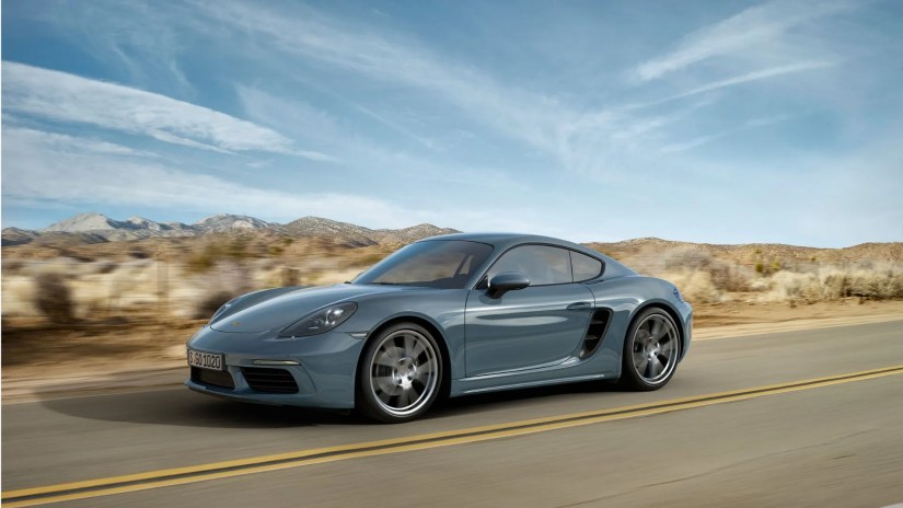 Front 3/4 view of a gray 2016 Porsche Cayman 718 driving on a road through the desert.