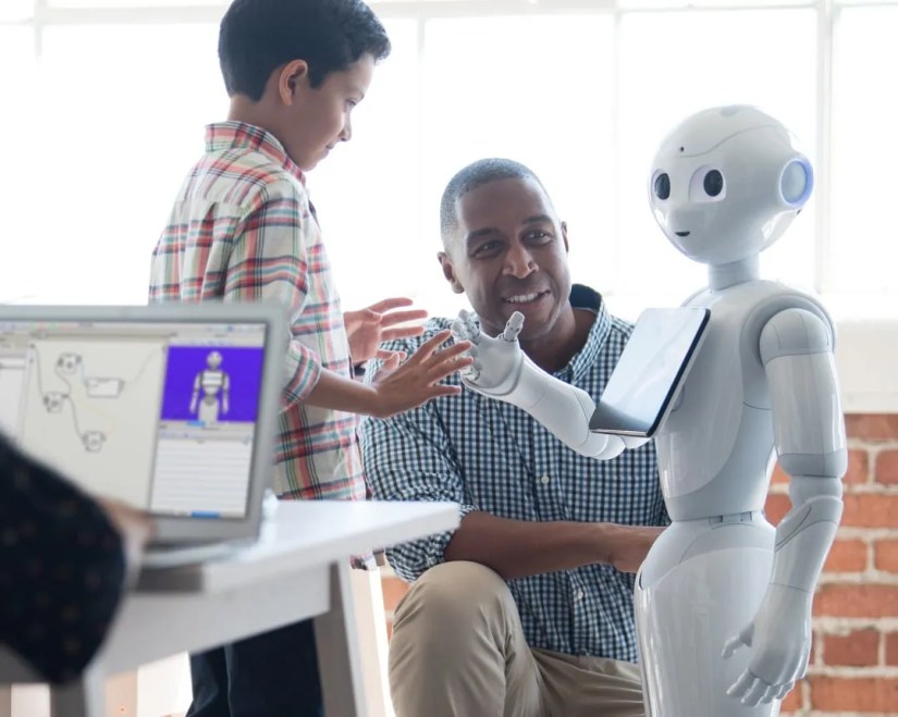 Pepper, a robot with rounded head, big eyes, and a tablet display on its chest interacting with a boy and a man.