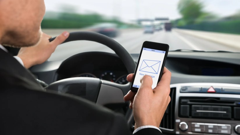 Close-up of a man holding cellphone with message notification while driving car.