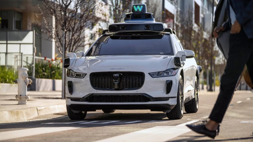 Front view of a Waymo Jaguar I-PACE stopping for a pedestrian crossing the road.