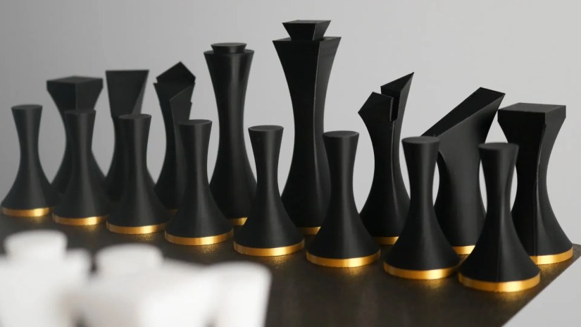 Minimalist 3D printed chess pieces in black and gold.