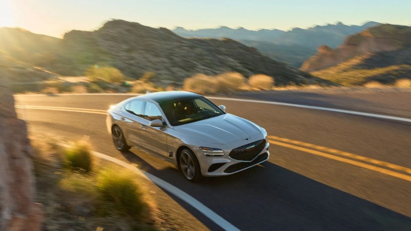Front 3/4 shot of a gray 2025 Genesis G70 driving on a winding country road.
