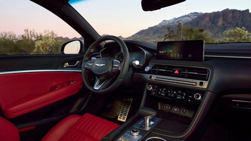 Close-up of the interior of a 2025 Genesis G70 showing the driver&rsquo;s seat, steering wheel, and infotainment screen.