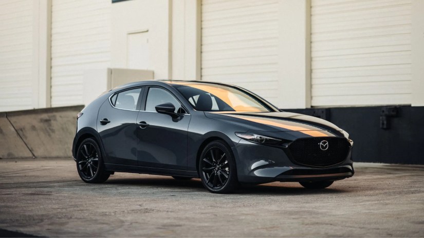 Front 3/4 shot of a black 2025 Mazda3 parked outside of a warehouse.