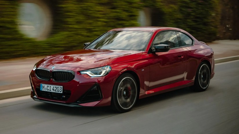 Front 3/4 shot of a red 2025 BMW M240i xDrive driving through a city.