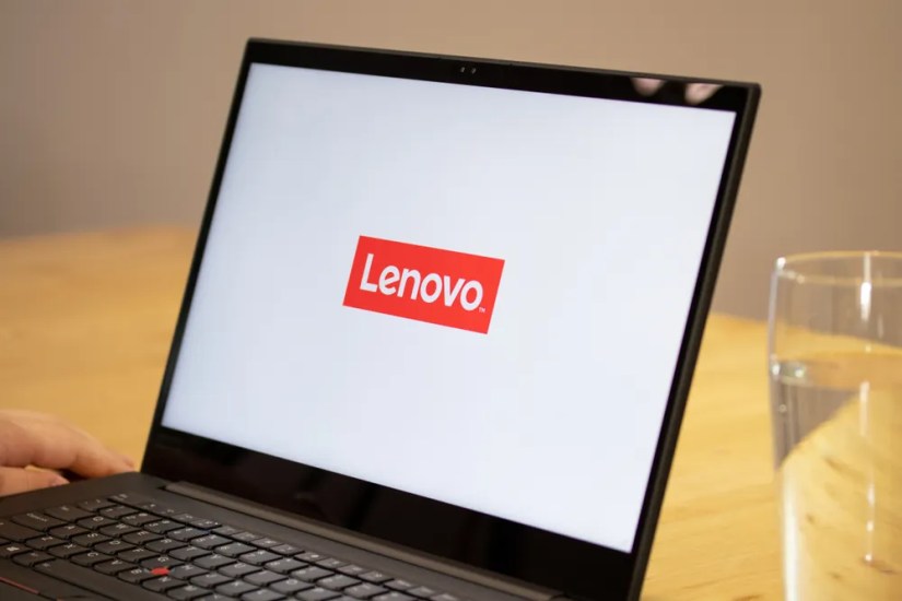Person sitting a desk using a Lenovo laptop with the Lenovo logo on-screen.