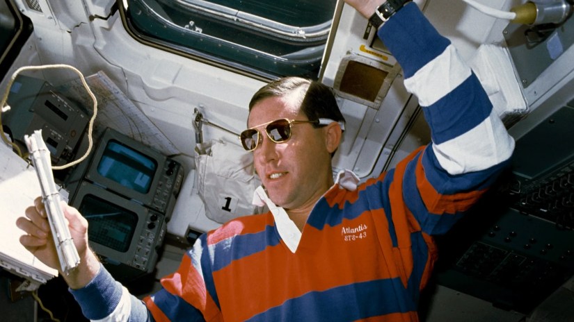 STS-43 Pilot Michael A. Baker, wearing sunglasses, reviews a checklist on the aft flight deck of Atlantis, Orbiter Vehicle (OV) 104.