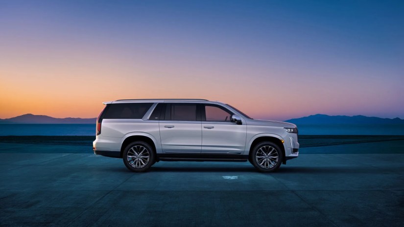 Static side profile shot of a white 2024 Cadillac Escalade ESV parked as the sun sets with mountains in the background.