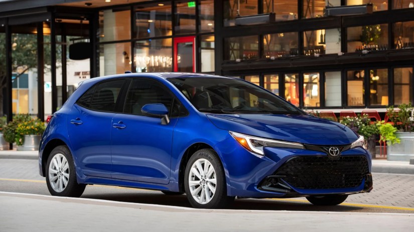 Static front 3/4 shot of a blue 2025 Toyota Corolla Hatchback SE parked in a city.