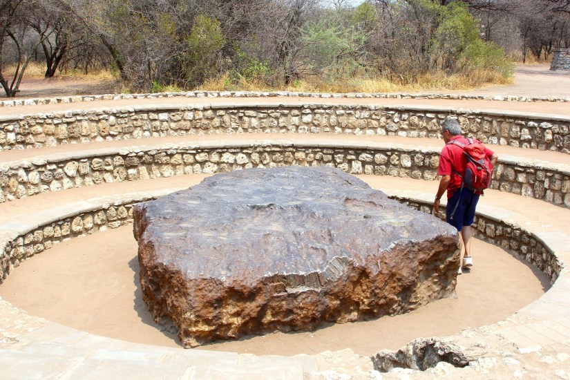 Man standing next to the prehistoric and ancient Hoba meteorite.