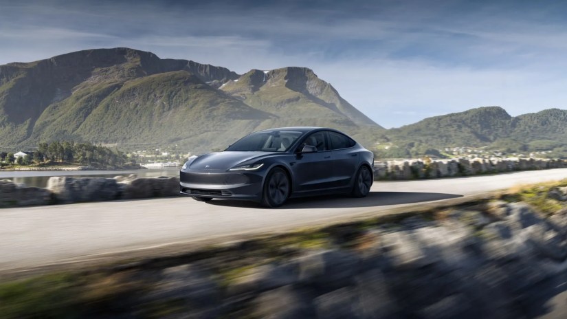 Dynamic front 3/4 shot of a gray Tesla Model 3 with mountains in the background.