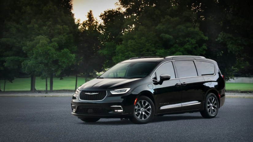 Static front 3/4 shot of a black 2025 Chrysler Pacifica Plug-in Hybrid Pinnacle with trees in the background.