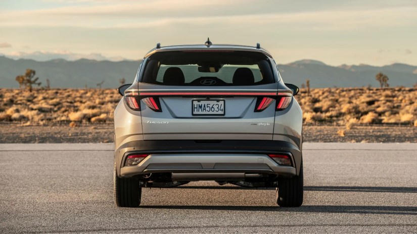 Static rear-end of a shot of a gray 2025 Hyundai Tucson PHEV parked on tarmac with mountains in the background.