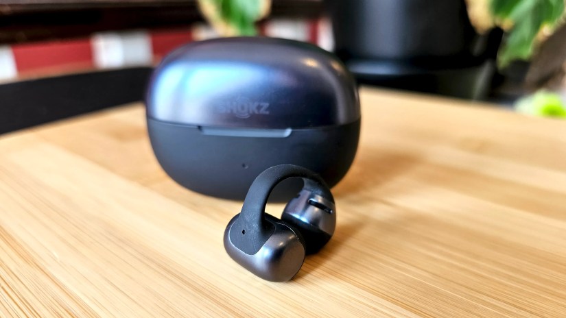 A single Shokz OpenDots One sitting in front of its charging case.