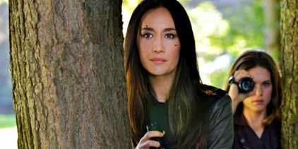 Maggie Q&rsquo;s Nikita behind a tree with another agent using a camera in Nikita