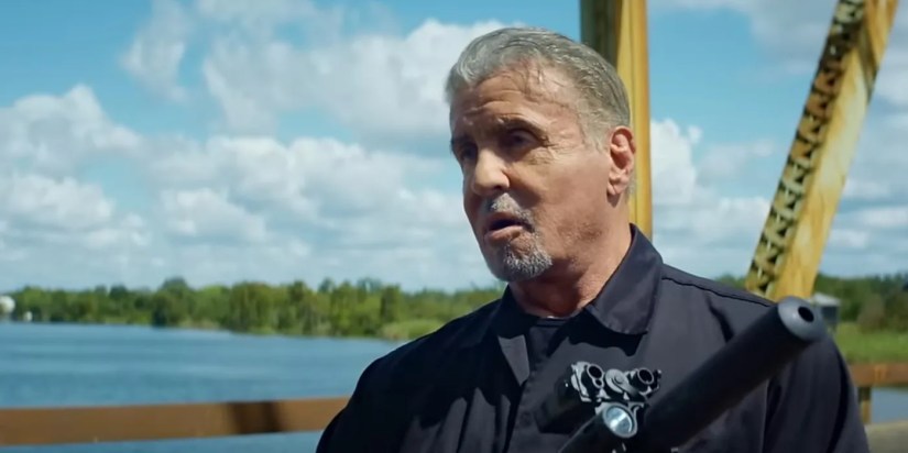 Sylvester Stallone Armor standing on a bridge holding a gun