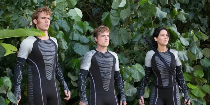 Katniss (Jennifer Lawrence), Peeta (Josh Hutcherson), and Finnick (Sam Claflin) standing in a jungle from the film Catching Fire