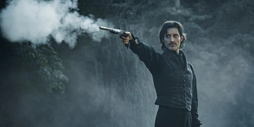 Pierre Niney as Edmond Dantès shooting a gun in The Count of Monte Cristo