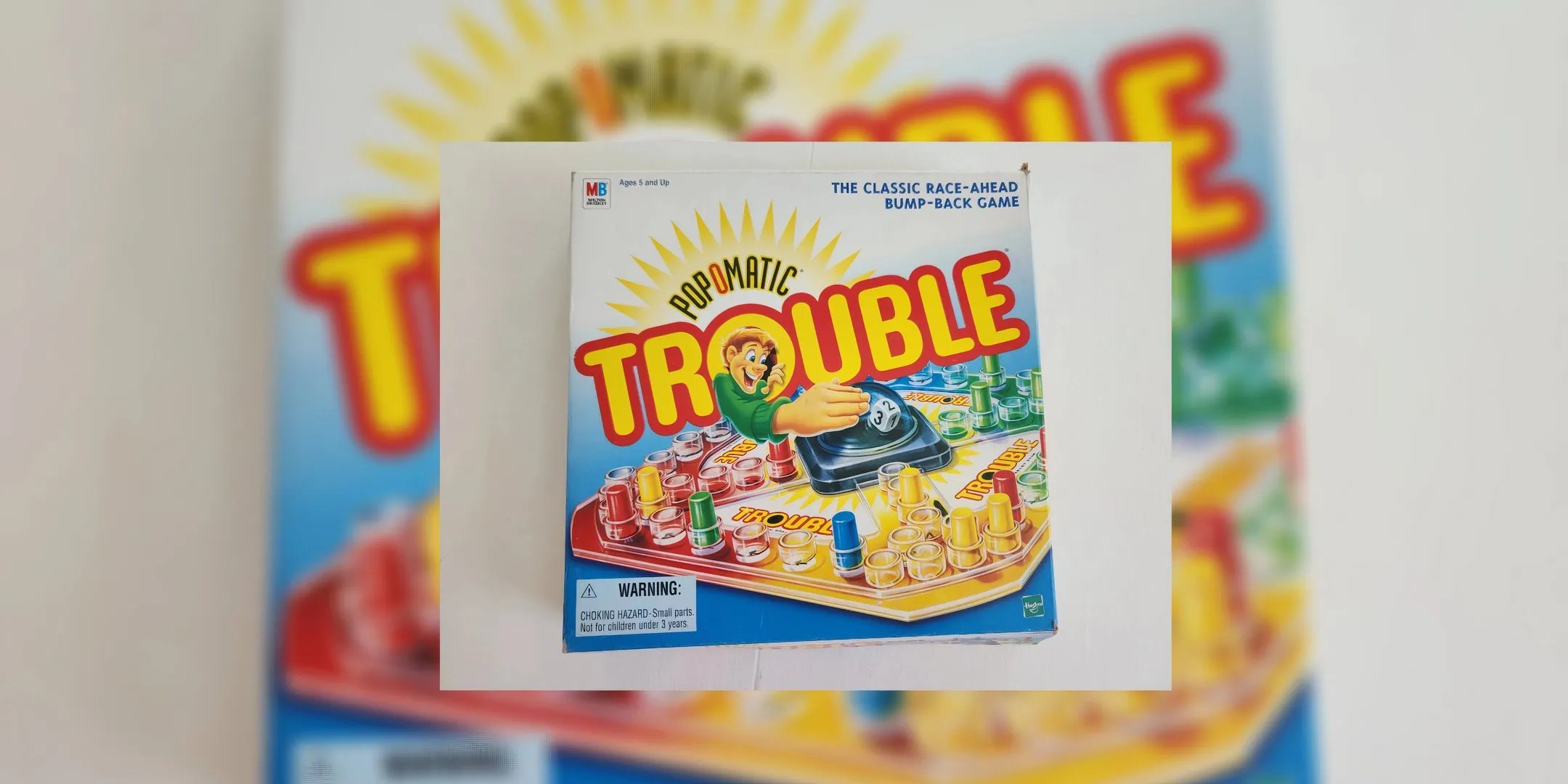 An animated man pokes out of the word Trouble to hit the Pop-o-Matic die in the center of the game board on the box cover.