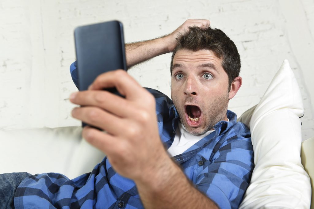 young attractive man lying at home couch using on mobile phone