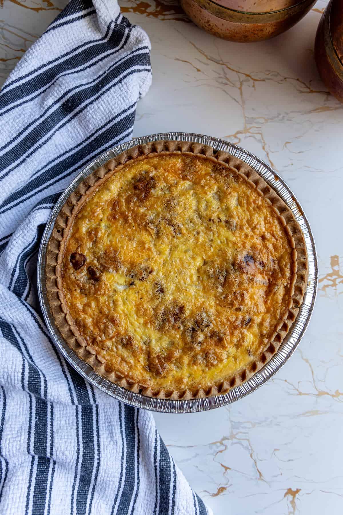 A bacon quiche is sitting on a table next to a towel.