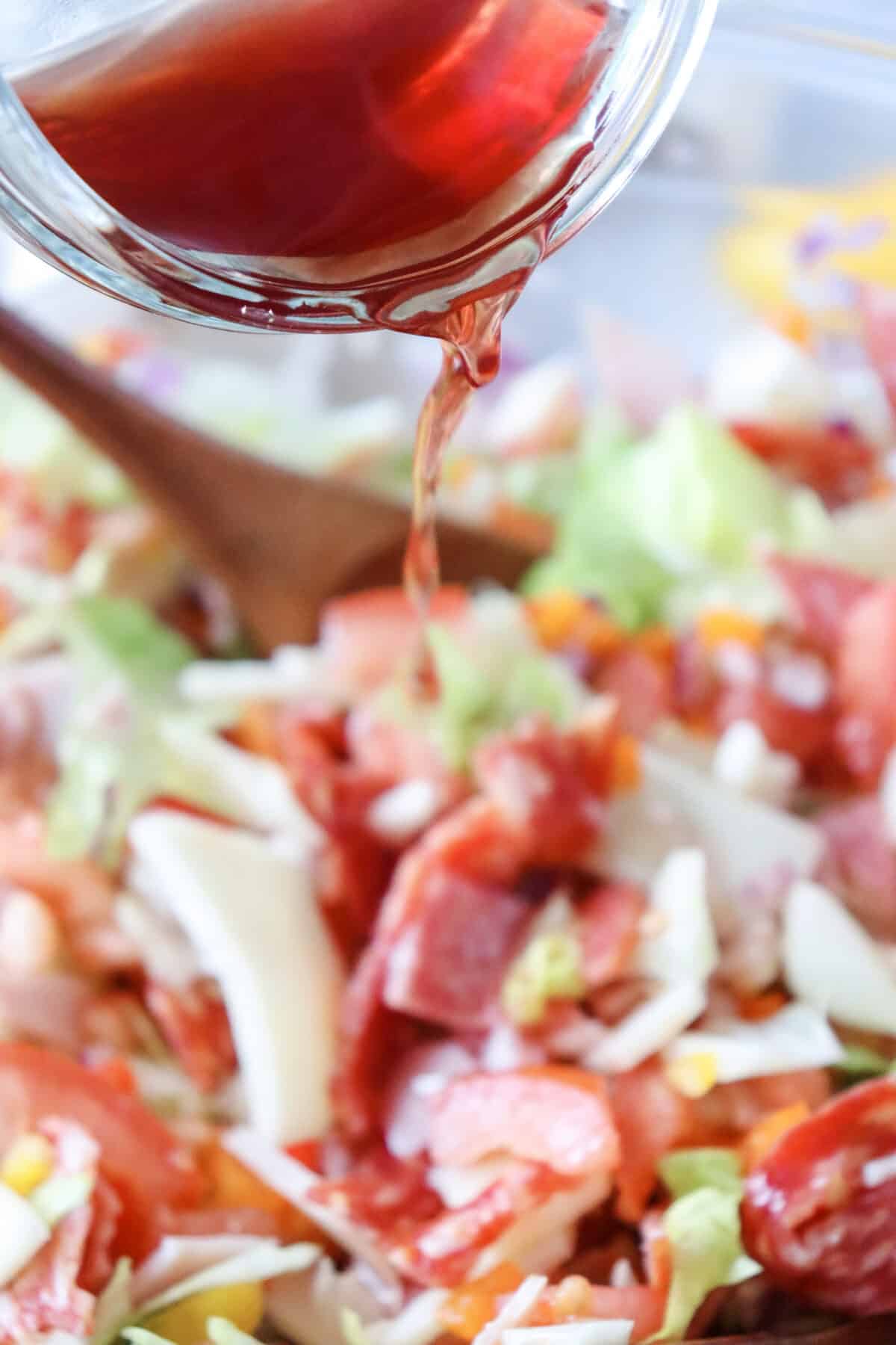 A spoon is being used to drizzle Italian sauce on a salad.