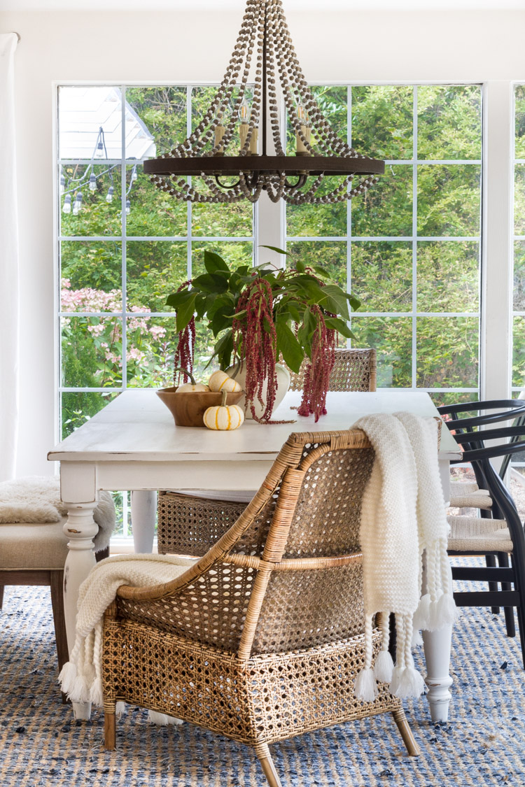 This farmhouse style dining room looks great with the touches of wicker, greens, and that gorgeous chandelier