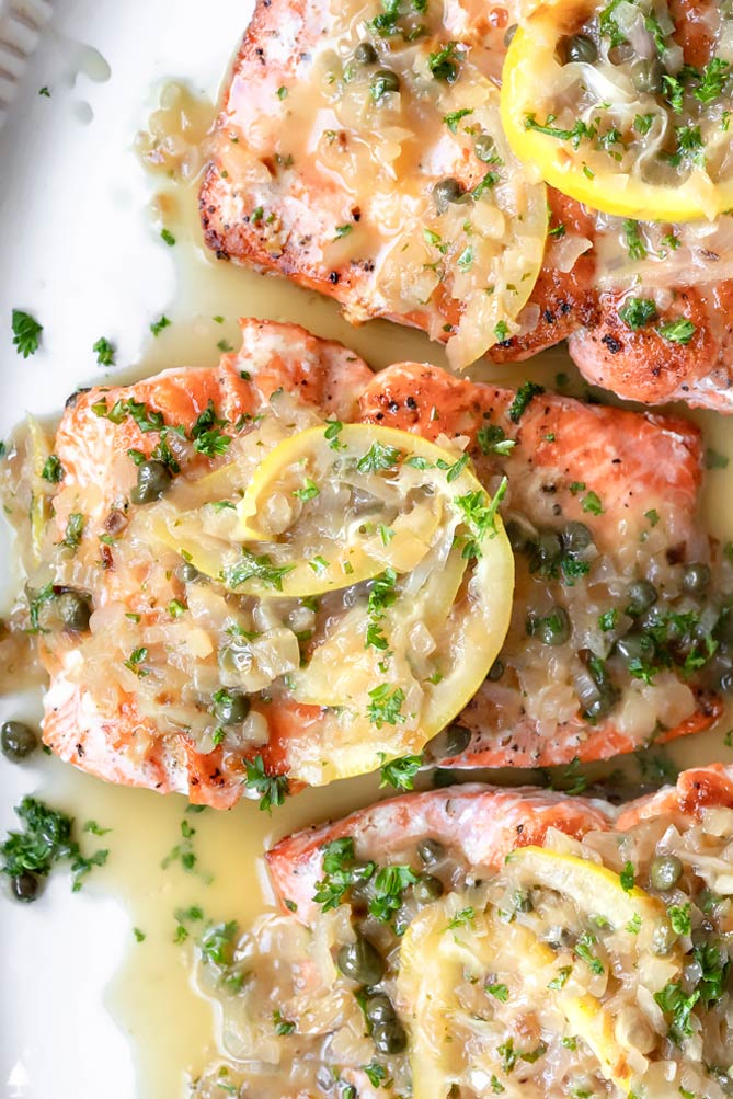 Tender, perfectly cooked fish, and a luxurious sauce spiked with capers, this salmon piccata makes an easy dinner feel extra elegant. #salmonpiccata #lowcarbsalmonpiccata top view of salmon piccata healthy topped iwth garnish