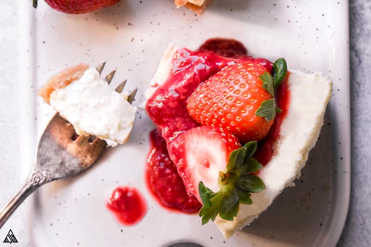 *NEW* There isn’t much more you can ask for from healthy desserts than this decadent low carb cheesecake recipe that is silky smooth with just the right amount of sweetness. #lowcarbcheesecake #ketocheesecake Slice of low carb cheesecake with strawberries on top