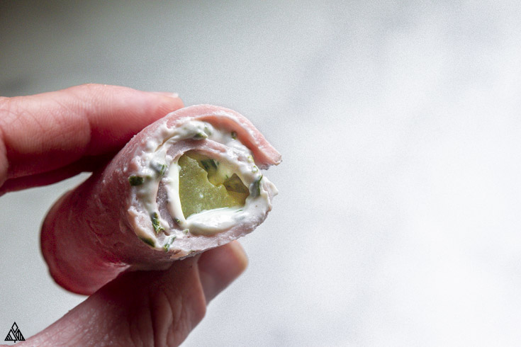 These ham roll ups make for mouthwatering and addictive snacks. Creamy cheese and tangy pickles pair perfectly with this salty ham, and you guys, they just look so fancy! #hamrollups #lowcarbhamrollups hand holding a piece of ham roll ups