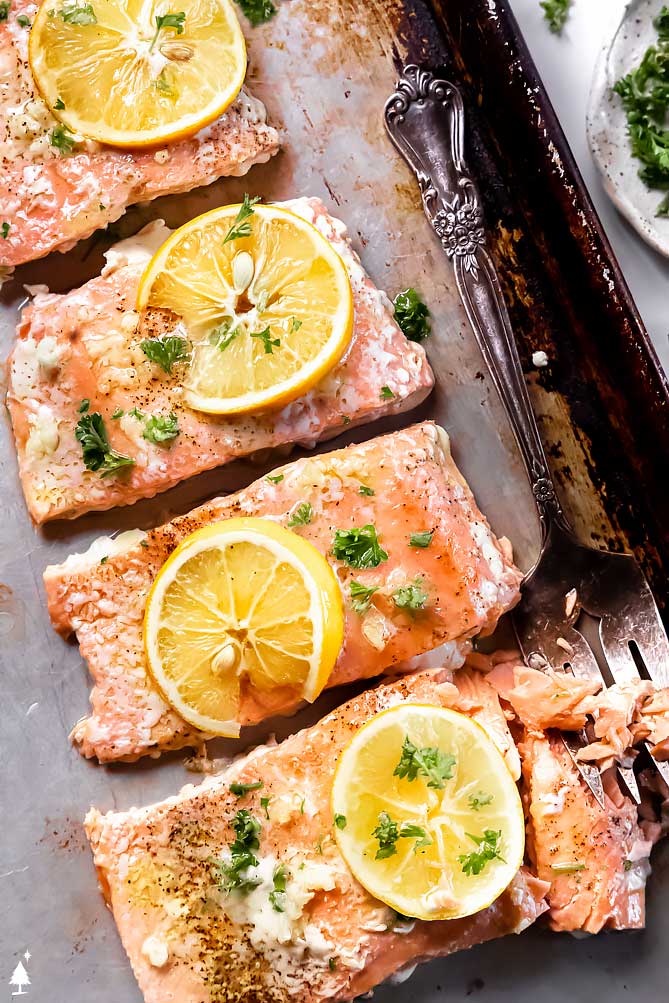 *NEW* How to bake salmon that's flakey, moist, and tender. Every. Time. This garlic and olive oil garnished fish only takes 5 minutes of prep! #bakesalmon #lowcarbbakesalmon closer view of best baked salmon recipe in the world on a pan