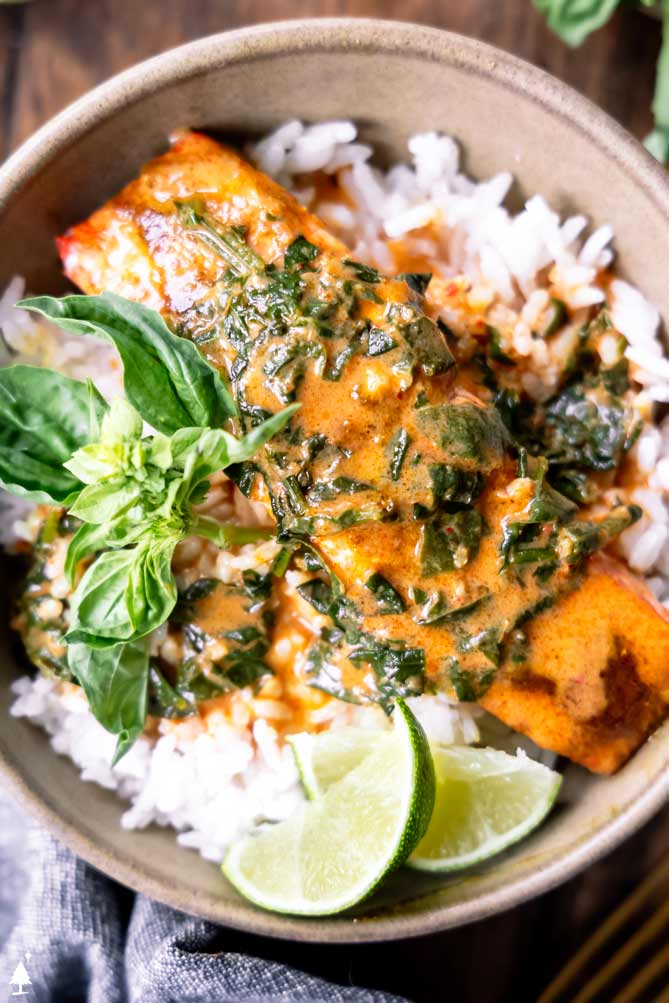 a bowl of thai salmon curry over rice with limes